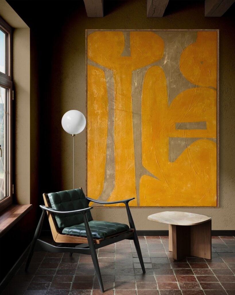 ყვითელი აბსტრაქტული ნახატი მუქ კედელზე და თანამედროვე სავარძელი